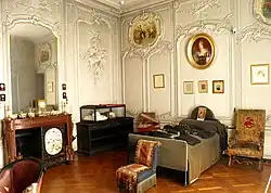 salle couverte de boiseries blanches, avec contre les murs, une cheminée, une vitrine et un lit surmonté d'un portrait. Trois fauteuils sont disposés au centre de la pièce