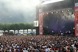 Photographie en couleurs d'une scène et du public d'un concert en plein air.