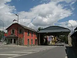 Vue d’un bâtiment aux murs rouges adossé à un préau surplombant une route.