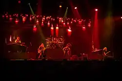 Cinq membres d'un groupe de rock jouant devant un écran projetant des bougies