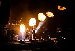 Trois membres d'un groupe de rock jouant sur scène avec de la pyrotechnie