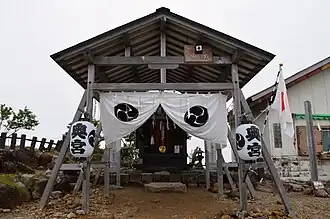 Photo couleur d'une structure en bois ouverte et sommairement décorée, avec un ciel laiteux en arrière-plan.