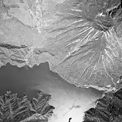 Photo noir et blanc d'un lac au pied d'un volcan, vu du ciel.