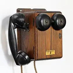 Un boitier en bois. Sur le dessus de petites coupoles noires, sans doute la sonnette. Accroché sur le côté, le combiné du téléphone.