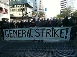 Groupe de manifestants massés à un carrefour et portant une banderole General Strike!