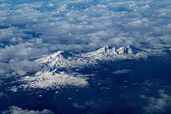 Vue aérienne de quatre sommets enneigés dépassant d'une mer de nuages sur l'un de leur versant.