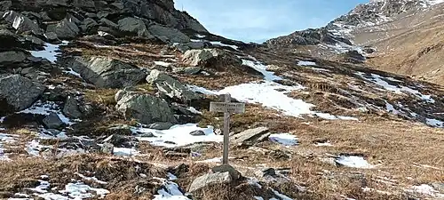 Photographie de la Combe Noire avec un panneau homonyme enneigée ; le paysage est automnal avec des névés et de l'herbe sèche.