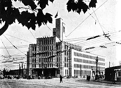 Photo d'un bâtiment important. Les rangées de fenêtres sont régulières et parfaitement alignées ; au premier plan, on devine les câbles d'un tramway.