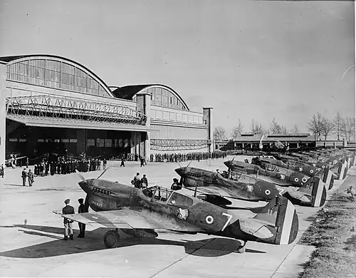 Photo noir et blanc de douze chasseurs Curtiss alignés sur un aérodrome devant un groupe d'officiels