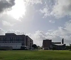 Photographie à contre-jour de deux bâtiments sous un ciel nuageux. Une étendue de pelouse s'étend au premier plan.