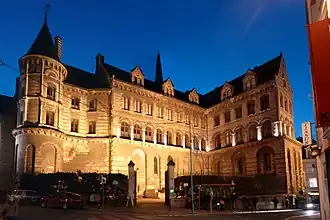  Photographie d'un imposant bâtiment médiéval, en tuffeau, éclairé la nuit. Une tour sur sa gauche