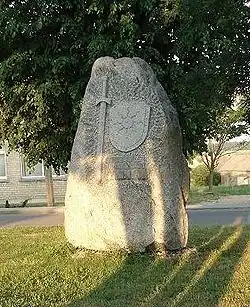 Stèle en pierre sur une pelouse, représentant une épée et un écu avec un soleil