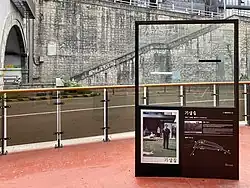 Photo d'un escalier donnant accès à un tunnel, situé derrière une plaque de verre qui donne des informations sur le tournage de Parasite.