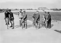 Quatre cyclistes sur leur vélo au départ d'une course sur un vélodrome, chacun tenu par un homme debout.