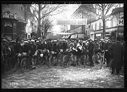 Photographie en noir et blanc de coureurs cyclistes sur une place.