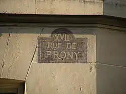 Plaque de rue (non réglementaire) de la rue de Prony, à l’angle de la rue Henri-Rochefort.