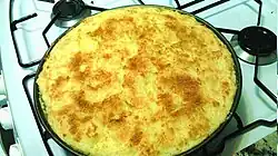 Plat rond de pastel de papa posé sur une plaque de cuisson au gaz et montrant la couche de fromage râpé gratinée de couleur jaune orangé