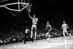 Joueur de basket-ball, sautant en l'air, tenant le ballon de sa main droite, pour le déposer dans le panier.