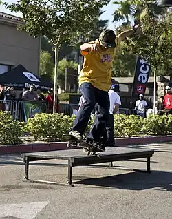 L'image montre un skater en train d'exécuter la figure 5-0 Grind : il grinde sur l'axe arrière, sur un rail.
