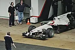 Photographie d'une monoplace blanche sortant des stands, vue de haut, de trois-quarts