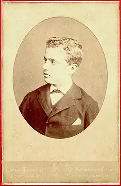 Photographie en noir et blanc d'un garçon en buste et de profil portant une veste foncée et une chemise claire. Il regarde vers sa droite.