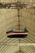 Vue en contreplongée d'une maquette suspendue à une poutre. Deux grands tangons en position levée de chaque côté du mât.