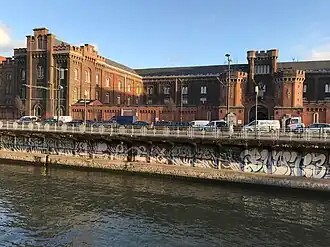 Photographie d'un bâtiment en brique vu depuis la rive d'un canal.