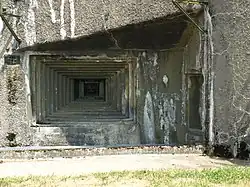 photographie en couleur d’un mur en béton percé d’une ouverture de tir