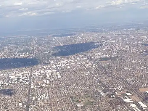 Photographie aérienne cadrée sur une agglomération entourée de zones montagneuses, où les zones urbaines sont clairement différenciées.