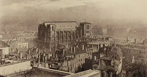 Photographie sépia d’une cathédrale dominant un quartier urbanisé, le tout dans la brume.