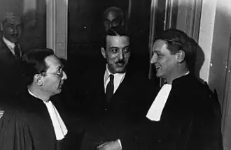 Dans un couloir du Palais de Justice, Bonny, souriant, plaisante avec ses deux avocats.