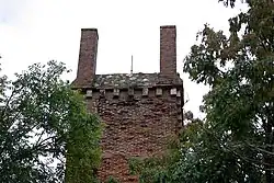 Vue du sommet d'un édifice en briques, couronné à chacun de ses angles d'une colonne de section carrée en briques.