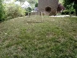 Vue en surplomb d'une terrasse engazonnée portant un cadre en bois et en contrebas, la base d'un monument.