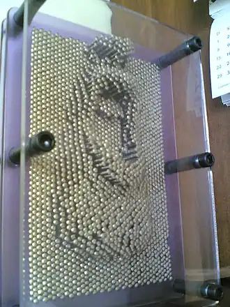 Un Pin Art de taille standard, avec en relief la moitié inférieure d'un visage.