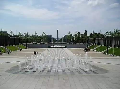 Perspective monumentale de la place de la Liberté, ouvrant sur la rue de Siam, avec la rade en arrière-plan, et sur la droite, le clocher de l'église Saint-Louis dépassant du centre reconstruit.