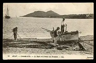Carte postale noir et blanc. Barque sur la grève avec un deux mâts dans une baie bordée de montagnes.
