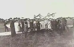 Photo en noir et blanc d'un avion sur le dos, entouré de plusieurs personnes.