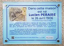 Plaque bleue en plexiglas portant un petit texte et deux photos de Lucien Péraire.
