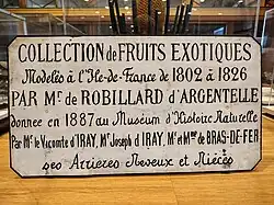 Plaque blanche avec un texte en noir commémorant le don de la collection de fruits en cire de Robillard d'Argentelle au Muséum d'histoire naturelle en 1887.