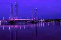 Photographie du pont Jacques Chaban-Delmas de nuit. La nuit est éclairée par le pont, qui reflète des couleurs violettes dans l'eau de la Garonne.