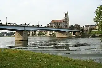 Vus depuis l’île aux Dames, le pont Neuf de Mantes, en béton et métal, et en arrière-plan la collégiale Notre-Dame de Mantes-la-Jolie. La fin de la dernière reconstruction du pont Neuf date de 1951.