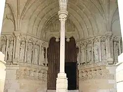 Photographie en couleurs du portail d'une église surmonté d'un tympan en ogive, colonne au premier plan.