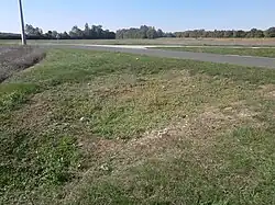 Photographie en couleurs d'un rectangle de pierres à demi dissimulées par de l'herbe rase