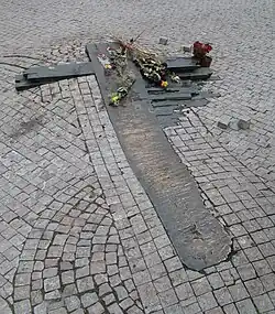 Une croix stylisée au sol, entourée par les pavés du sol, avec des roses.