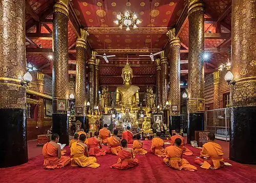Bhikshus assis devant une statue de Bouddha dorée pendant l'heure de la prière à l'intérieur du Wat Mai Suwannaphumaham, temple bouddhiste du 18e&nbsp;siècle, devant une statue de Bouddha dorée, à Luang Prabang. Septembre 2023.