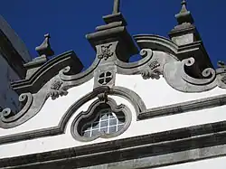 Photographie en couleurs. Gros plan sur le fronton blanc au relief couleur de pierre.