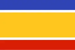 Drapeau composé de 5 bandes horizontales : large bande jaune au centre, encadrée de fines bandes blanches, puis bande moyenne bleue en haut, et également moyenne bande rouge en bas.