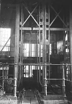 Photo noir et blanc montrant une cage d’ascenseur, la base du chevalement et l'orifice du puits.