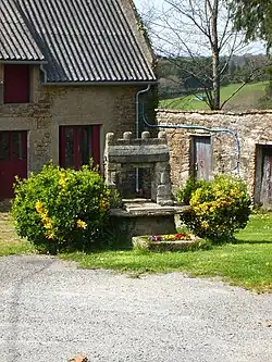Photographie en couleurs d'un puits en pierre dans un hameau.
