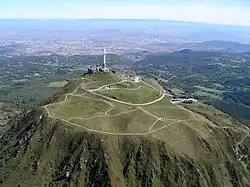 Vue aérienne du puy de Dôme depuis l'ouest avec Clermont-Ferrand au second plan et, à l'horizon, le mont Blanc, distant de 315&nbsp;km.